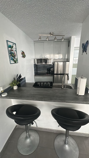 Una cocina moderna con una isla central, electrodomésticos de acero inoxidable y una zona de asientos con taburetes negros.