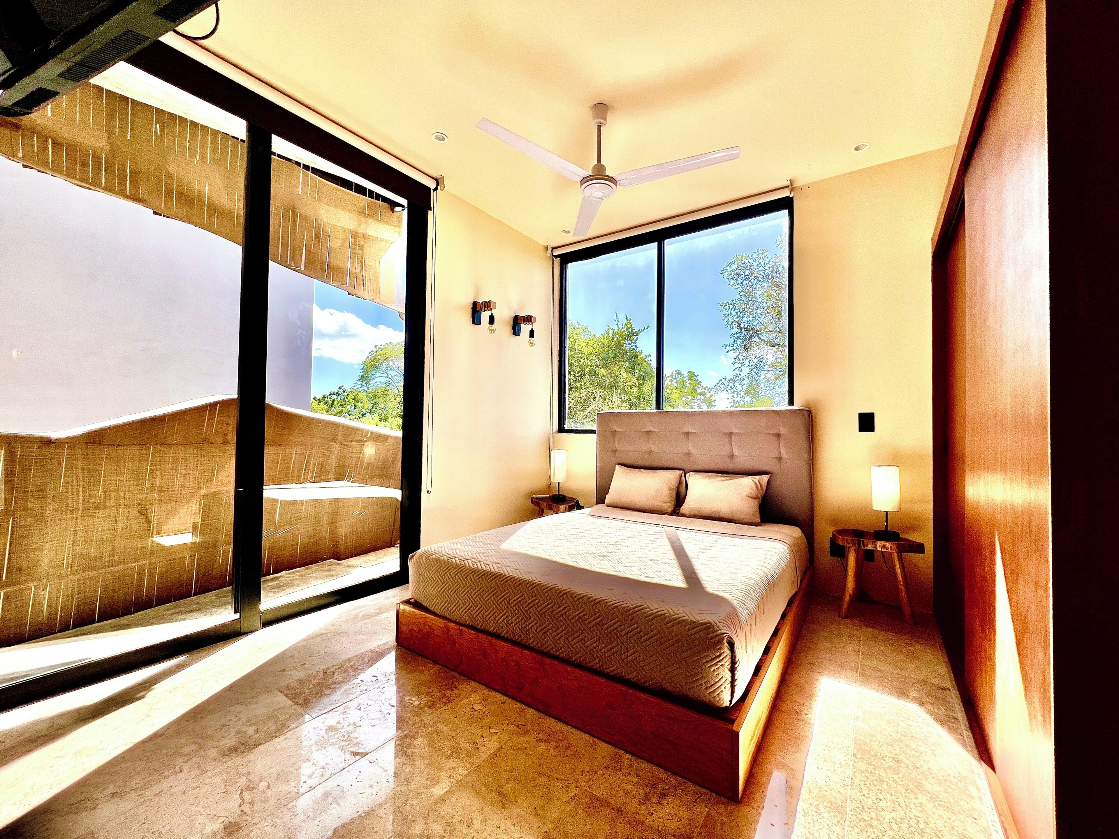 A bedroom with a bed, a ceiling fan, a window, and a view of the outdoors.