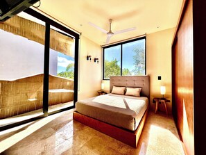 Ein Schlafzimmer mit Bett, Deckenventilator, Fenster und Blick ins Freie.