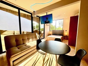 Ein modernes Hotelzimmer mit Sofa, rundem Tisch, Bett, Fernseher und großen Fenstern.