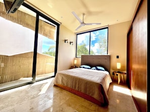 Ein Schlafzimmer mit einem Bett, einem Deckenventilator, einem Nachttisch, einem Fenster mit Blick und einer Schiebetür.