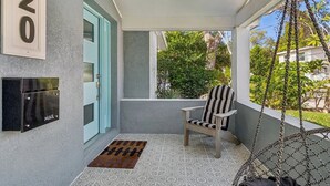 Varanda com caixa de correio, porta, cadeira e balanço pendurado.