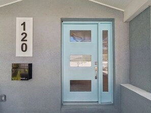 A light blue door with a mail slot and a number '120' sign on the wall.