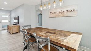Uma sala de jantar com uma mesa de madeira comprida, cadeiras de metal e luminárias pendentes.