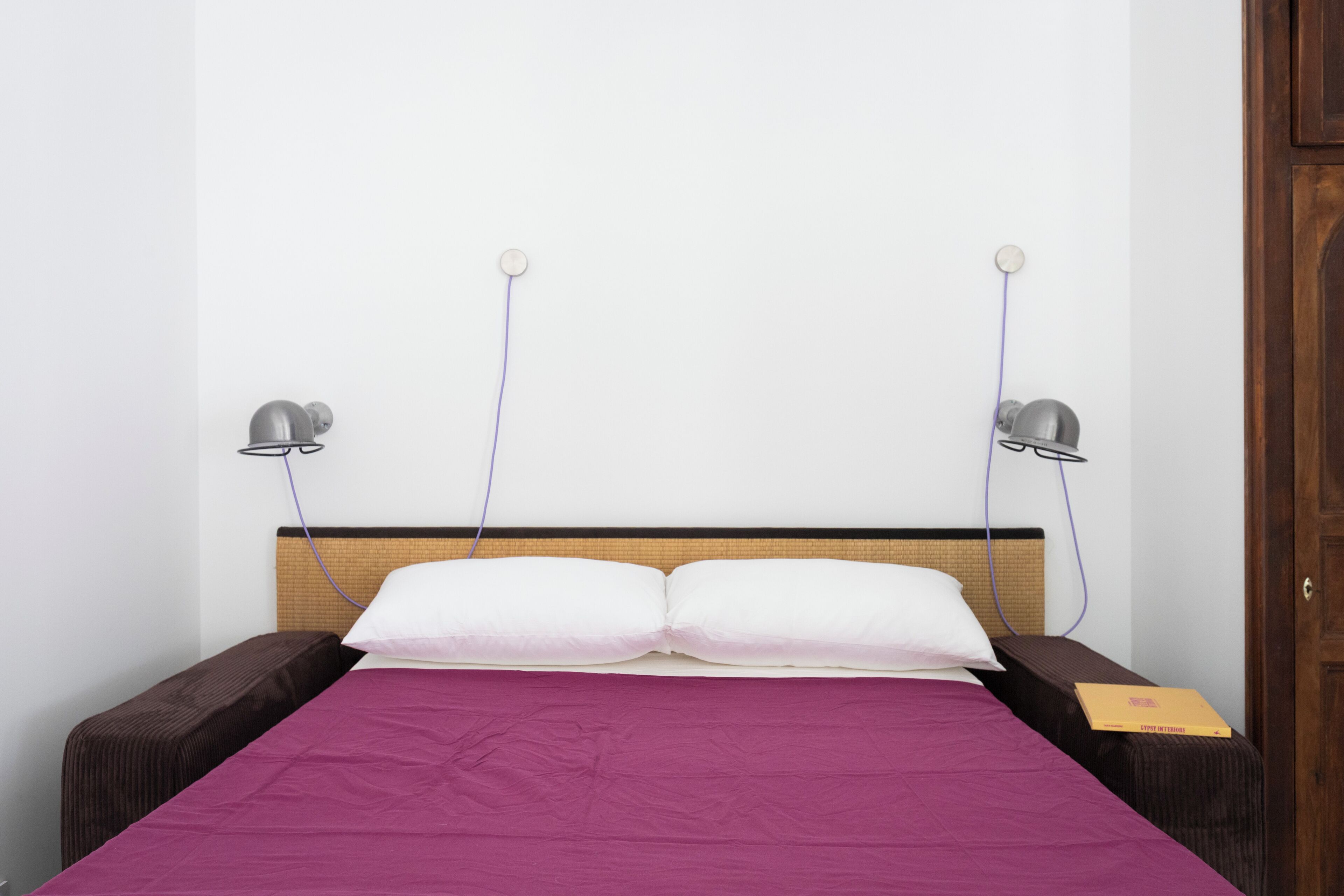 Ein Bett mit violettem Überwurf, zwei Nachttischlampen und einem Holzkopfstück.