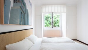 Ein Hotelzimmer mit Bett, Fenster mit Blick auf Grünflächen und einem gerahmten Bild an der Wand.