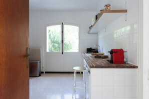 Eine Küche mit Fenster, Heizkörper, einem roten Gerät und einem Hocker.