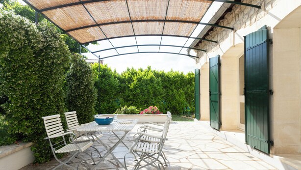 Eine Terrasse im Freien mit Tisch und Stühlen, einem überdachten Bereich und einem Steinboden.