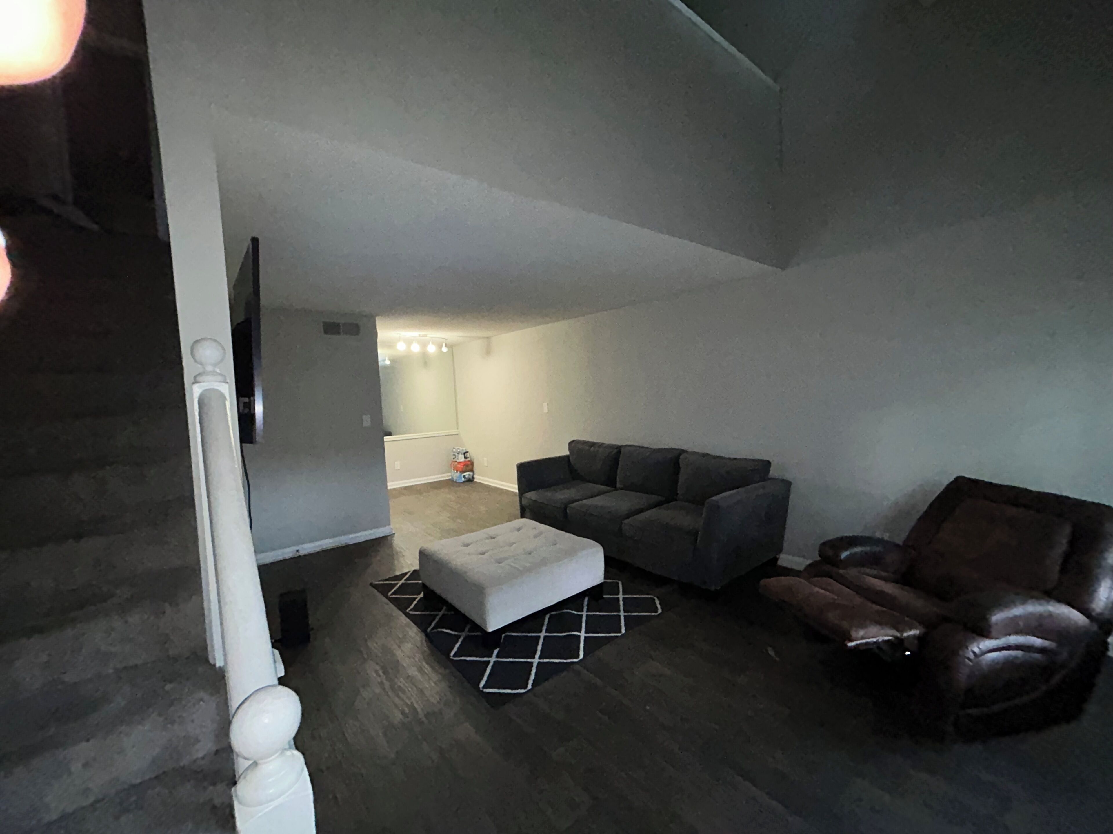 Un salon moderne avec un canapé gris, un fauteuil en cuir et un pouf blanc.