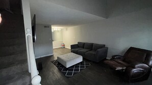 Un salon moderne avec un canapé gris, un fauteuil en cuir et un pouf blanc.