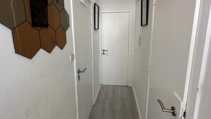 Un pasillo con suelo de madera, paredes blancas y elementos decorativos hexagonales en la pared. Hay dos puertas a cada lado, una con pomo y otra con palanca.