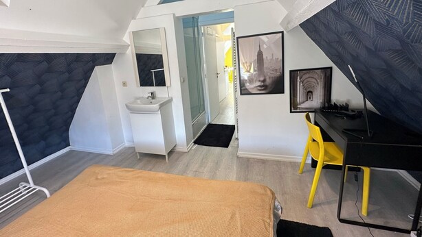 Un dormitorio con cama, escritorio, silla, lavamanos y espejo.