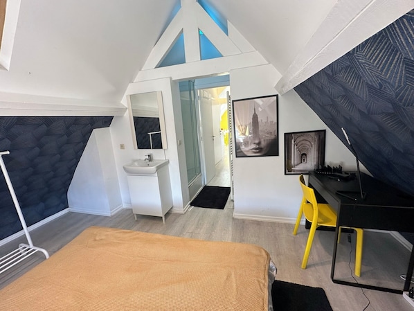 Ein Schlafzimmer mit Bett, Schreibtisch, Stuhl, Waschbecken und Spiegel.