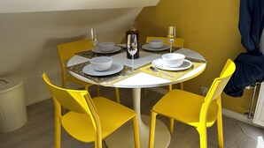 Comedor con mesa redonda, sillas amarillas, platos blancos, tazones y una botella de vino.