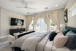 Ein Schlafzimmer mit Bett, Fernseher, Deckenventilator und einem Fenster mit Vorhängen.