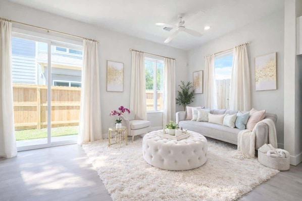 Ein geräumiges Wohnzimmer mit einem weißen Sofa, einem runden Hocker und einem Deckenventilator.