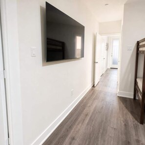 Ein Flur mit an der Wand montiertem Flachbildfernseher, Holzboden und einer Tür zu einem weiteren Zimmer.