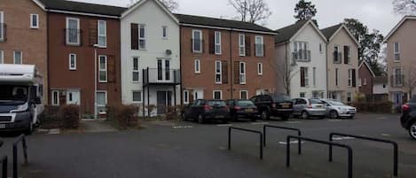 Una zona residencial con varias casas de dos pisos, un estacionamiento con varios automóviles y una camioneta blanca estacionada al costado.