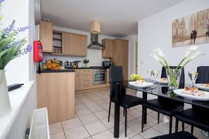 A modern kitchen with wooden cabinets, a central island, and a dining area with black chairs and a glass table. - Beautiful 4 Bedroom House Berkshire - Free Parking (Bracknell)