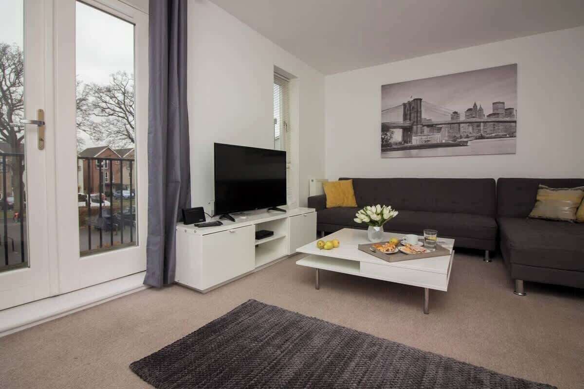 Ein modernes Wohnzimmer mit einem Flachbildfernseher, einer Couch, einem Couchtisch mit Speisen und einem Stadtbildgemälde.