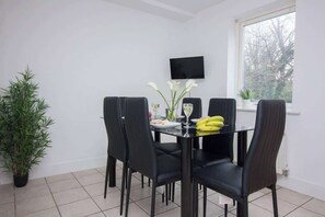 Ein Essbereich mit einem Glastisch, schwarzen Stühlen, einer Topfpflanze und einem Fenster mit Blick.