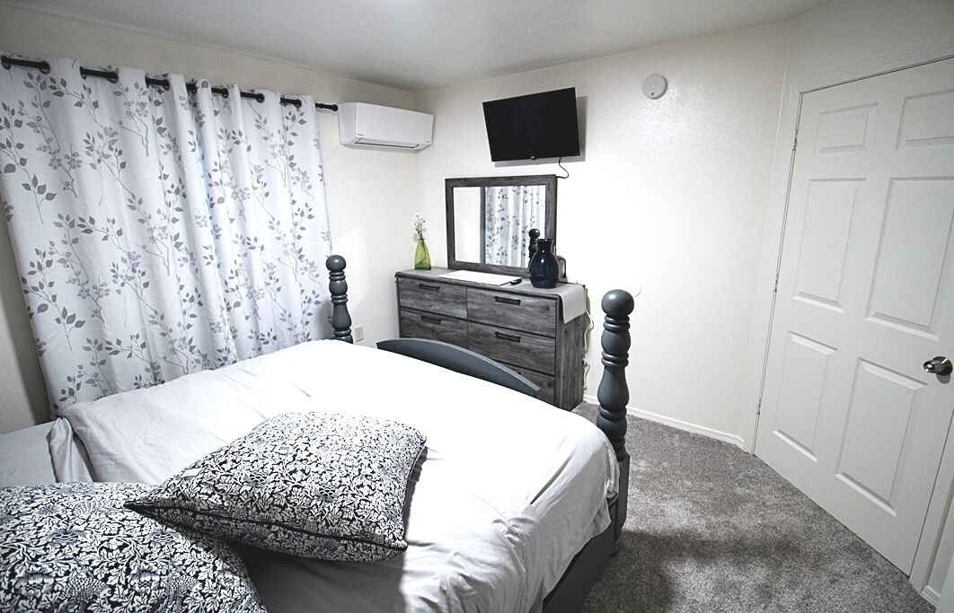 Une chambre à coucher comprenant un lit, une commode, un téléviseur fixé au mur et une porte.