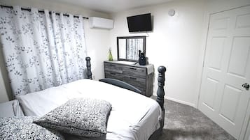 Une chambre à coucher comprenant un lit, une commode, un téléviseur fixé au mur et une porte.