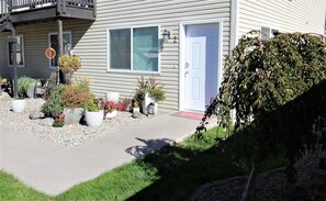 A residential building with a front porch, potted plants, and a well-maintained lawn.