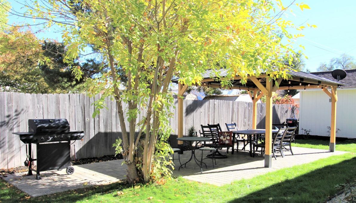 A backyard with a wooden pergola, a barbecue grill, and a dining table with chairs.