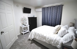 Un dormitorio con cama, cómoda, televisor y ventana con cortina.