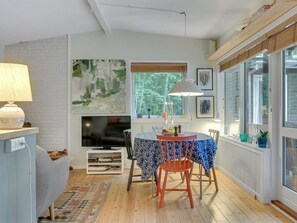 Ein gemütliches Zimmer mit Kamin, einem Esstisch mit Stühlen, einem Fernseher und einem großen Fenster mit Jalousien.