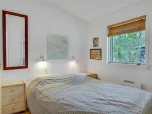 Quarto com cama, mesas de cabeceira, janela com vista para árvores e obra de arte na parede.