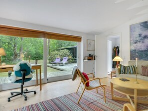 Ein modernes Wohnzimmer mit einem großen Schiebeglastür, die auf eine Terrasse führt, einem bequemen Sofa, einem kleinen runden Tisch und einem Sessel.
