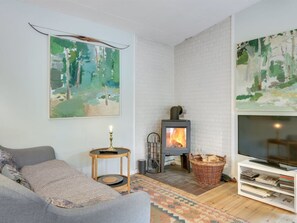 Ein gemütliches Wohnzimmer mit Kamin, einer Couch, einem Fernsehmöbel und einem Bild an der Wand.