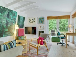 Ein modernes Wohnzimmer mit Fernseher, einem grünen Sessel, einem Schreibtisch und Kunstwerken an den Wänden.