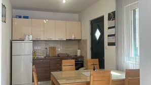 Eine kompakte Küche mit Kühlschrank, Herd und Schränken, ein Esstisch mit Stühlen sowie eine Tür mit Kalender.