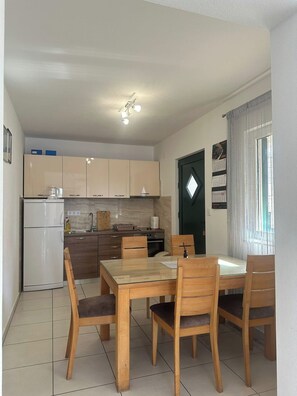 Eine kompakte Küche mit Kühlschrank, Herd und Schränken, ein Esstisch mit Stühlen sowie eine Tür mit Kalender.