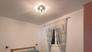 Ein Schlafzimmer mit einem Bett, einem Nachttisch, einem Fenster mit Vorhängen und einer Deckenleuchte.
