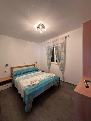 Ein Schlafzimmer mit einem Bett, einem Nachttisch, einem Fenster mit Vorhängen und einer Deckenleuchte.