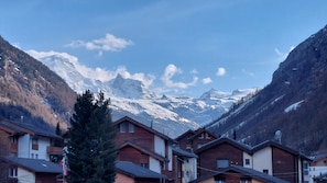 A mountain village with traditional wooden houses, a clear sky, and snow-capped peaks in the background. - Large apartment with panoramic view and free parking, 5 min from train station (Täsch)