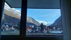 A view through a window of a residential area with houses and snow-capped mountains in the background. - Large apartment with panoramic view and free parking, 5 min from train station (Täsch)