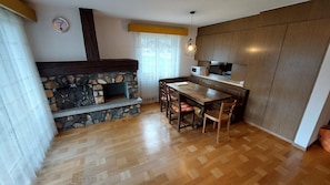A kitchen with a stone fireplace, wooden dining table, and chairs. - Large apartment with panoramic view and free parking, 5 min from train station (Täsch)