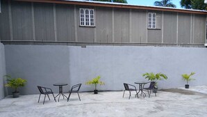 Un patio con mobiliario exterior, plantas en macetas y un edificio con amplias ventanas.
