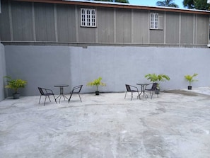 Un patio con mobiliario exterior, plantas en macetas y un edificio con amplias ventanas.