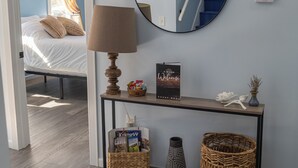 A hotel room with a bed, a bedside table with a lamp, a mirror, a framed welcome sign, a small basket, a vase, and a wicker basket. - Close to Mammoth Cave and other wonderful attractions yet still in a quiet area. (Horse Cave)