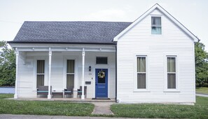 A white single-story house with a blue front door, a porch with wicker furniture, and a small window on the right side. - Close to Mammoth Cave and other wonderful attractions.  location. (Horse Cave)