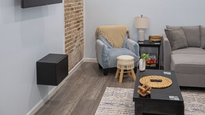 A modern living room with a flat-screen TV mounted on the wall, a grey sofa, a small wooden stool, a coffee table with a woven placemat, and a patterned rug. - Close to Mammoth Cave and other wonderful attractions yet still in a quiet area. (Horse Cave)