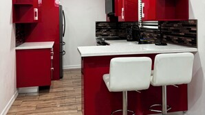 Una cocina compacta con armarios rojos, una encimera blanca y dos taburetes blancos.