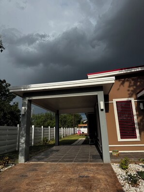 Uma área externa coberta com um caminho que leva a uma entrada de edifício, uma cerca branca e um céu nublado.