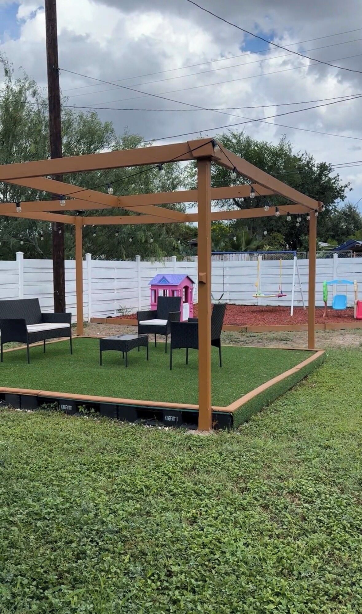 A gazebo structure with a metal frame and a roof, surrounded by artificial grass.